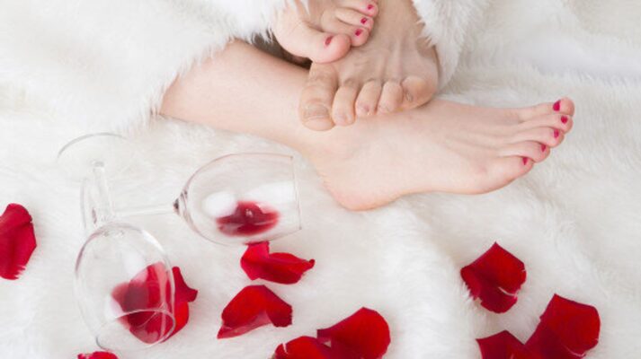 Raunchy Valentine's Day Gift Guide image of Two Wine Glass Rose Petals three Bare Feet on a White Fur.