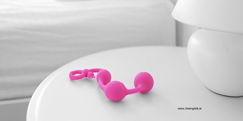 A Beginner's Guide To Anal Beads Pink Anal Beads Standing Beside a Bedside Lamp