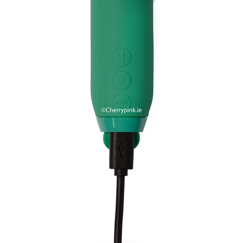 The green vibrator with its charging cable plugged into the base