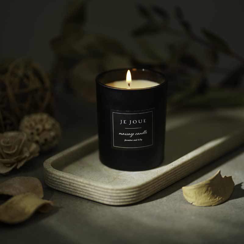 Je Joue Luxury Massage Candles Black lighting on a piece of wood.