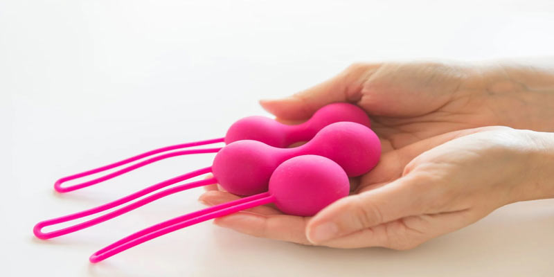 A Beginners Guide to Kegel Exercises image of a pair of hands holding three pink Kegel Balls.